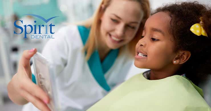 Little girl looking at teeth in mirror that the dentist is holding