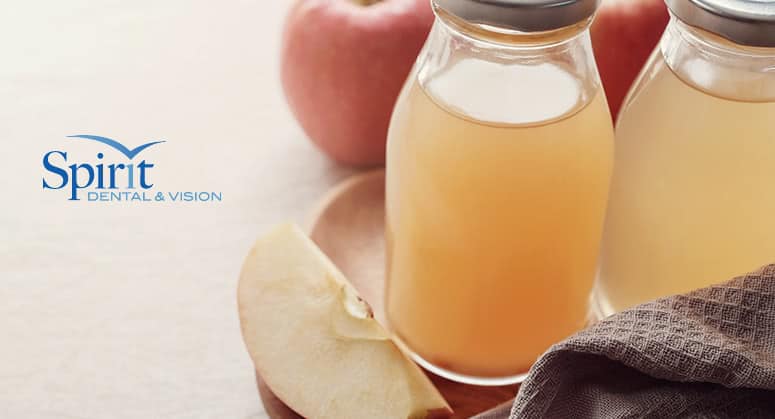 Bottles of apple cider vinegar (ACV) on table with sliced apples.