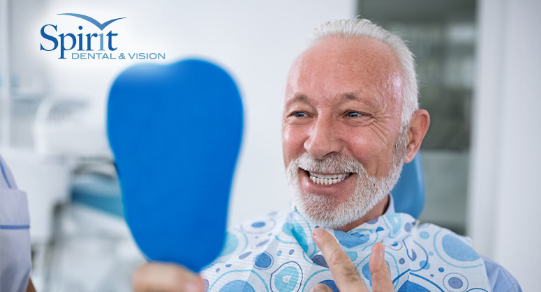 Older man smiling while looking at his teeth in mirror