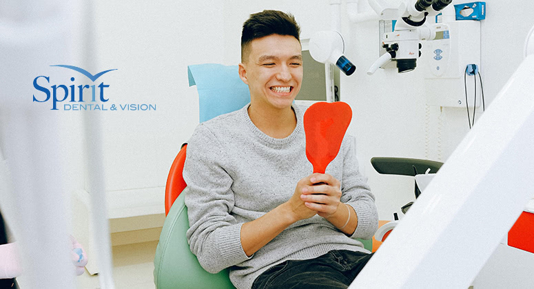 Young adult looking in mirror at dentist office and smiling