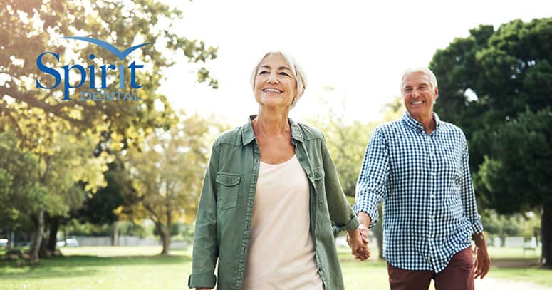 an elderly couple smiling, holding hands on a walk