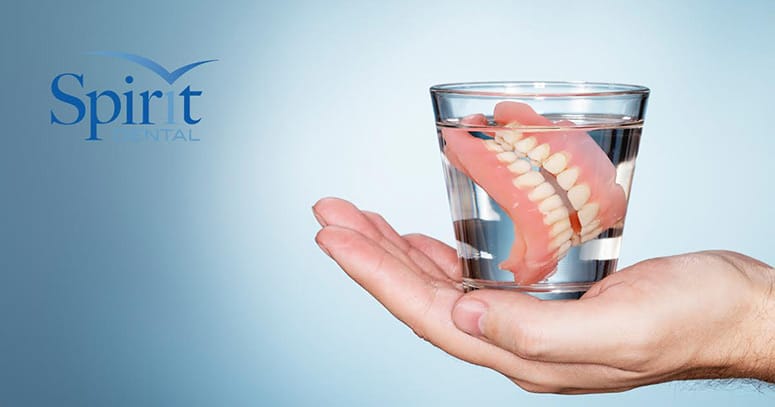 Sombody holding a water glass with dentures in it