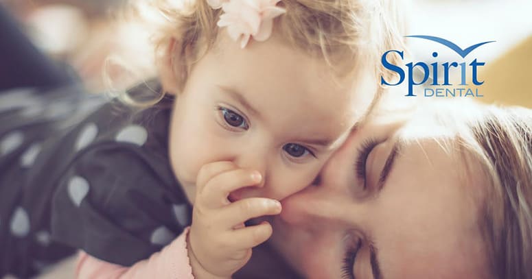 Mother kissing young daughter as she's sucking her thumb